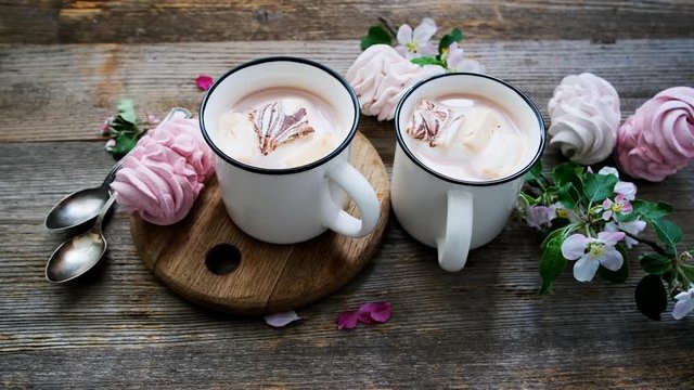 Tasty marshmallow and cups with cocoa near spring flowers
