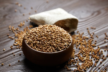 Buckwheat groats (hulled seeds) in bowl and burlap bag on wooden table