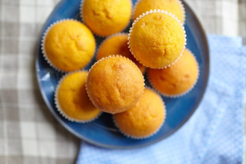 Pumpkin muffins on blue plate on table with tablecloth, top view. Homemade bakery, plant-based food