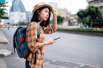 Asian female tourist Stand calling a taxi with an application on smartphone. Is a technology that facilitates his travel. While traveling in the capital.