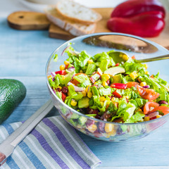 American-Mexican healthy salad with avocado, beans, corn, onions, lettuce and tomatoes in a glass bowl