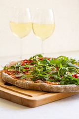 Pizza on rye pastry with mushrooms, tomatoes, ham, ramiro pepper, arugula and parmesan. Pizza served on a wooden board with white wine.