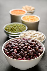 Sources of vegetable protein. Different types of legumes in bowls on a dark stone table. Vegan and vegetarian food concept. Vertical orientation.