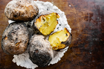 Baked in the fire potatoes in the skin according to the village recipe and method, directly in the ashes. Charred, fragrant tubers, a hot dish on a white stone plate