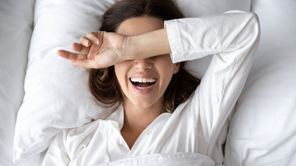 Cheery woman lie in bed woke up after sleeping, hide eyes from sunlight in morning, enjoy new day,...