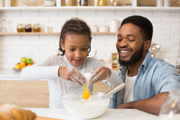Excited girl adding egg to cookies dough, cooking at kitchen