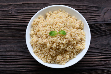 Bowl of boiled quinoa on wood background