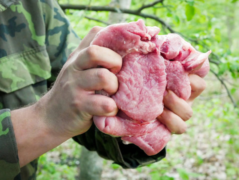 A man with both hands tightly squeezes a piece of fresh steak. Outdoors, close up