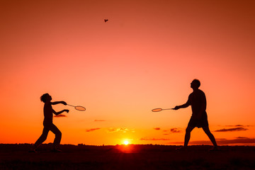 Fototapeta na wymiar Father and son playing badminton in the evening, silhouettes of people exercising in nature, recreation, sport, lifestyle concept 