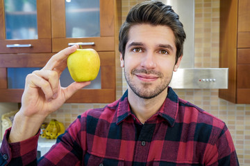 Young attractive cheerful male chef showing an apple in the kitchen wearing a shirt 