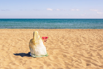 Back view of lonely Muslim woman  traveler in a colorful headscarf, scarf holding ripe of...