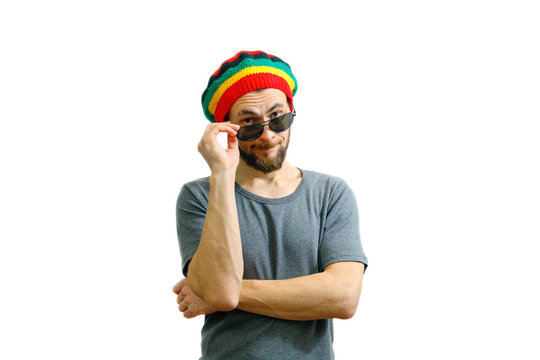 Young caucasian man in rasta hat and grey t-shirt holding sunglasses in hand
