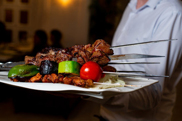 the waiter holds a plate with barbecue
