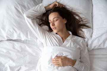 Top view gorgeous woman in white nightwear is in state of deep sleep, peaceful female lying sleeping relaxing under warm soft duvet asleep in comfortable bed, enjoy healthy rest sweet dreams concept
