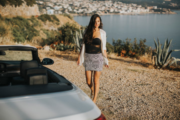 Young woman walking to cabriolet car at seaside