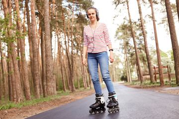 Picture of delighted glad good looking young woman rollerskating alone, being in middle of forest...