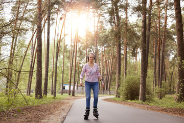 Horizontal picture of cheerful tender attractive young woman rollerskating, listening to music, being in forest, having rest, smiling sincerely, enjoying free time alone. Relax time concept.