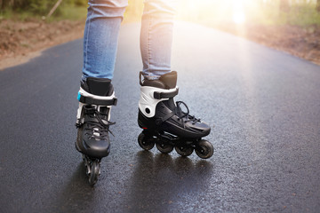 Horizontal picture of unknown person rollerskating, rollerskates being on wet road, having sun on...