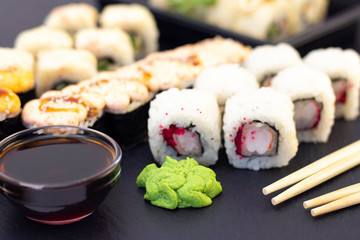 Set of rolls, wasabi, sauce and wooden sticks on a stone black table.