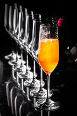 Composition with tall glass cocktail glass with orange cold drink, ice cubes melting on a dark shiny surface on a deep black background