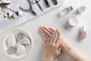 woman's hands with delicate pink manicure on the background of manicure tools. nails salon and spa. White concrete background, top view.