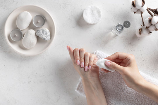 young woman removing pink nail polish with remover liquid. Personal hygiene and care concept. White concrete background, flat lay.