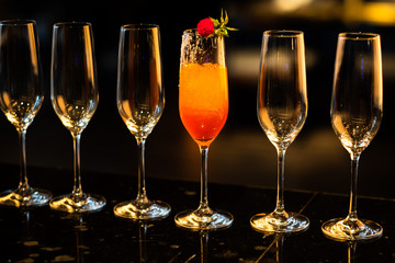 Composition with tall glass cocktail glass with orange cold drink, ice cubes melting on a dark shiny surface on a deep black background