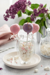 pink and lilac cake pops in a glass with marshmallows on a background of a bouquet of flowers. concept for birthday, wedding and holiday. vertical image.