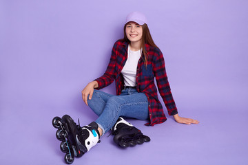 Indoor shot of happy smiling lady sitting on floor in skating roller, being ready to spend time in...