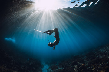 Free diver woman with fins glides over coral bottom and amazing sun rays. Freediving underwater in...