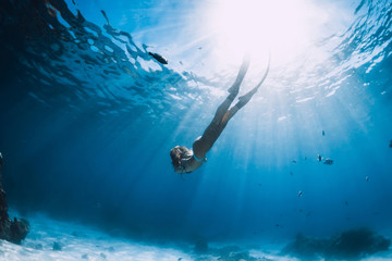 Fototapeta na wymiar Woman free diver with fins glides over sandy bottom near corals underwater in blue sea