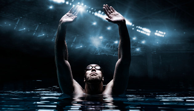 Swimmer in the pool raises his hands up. Water Sports Victory Concept. Arena with flashes.
