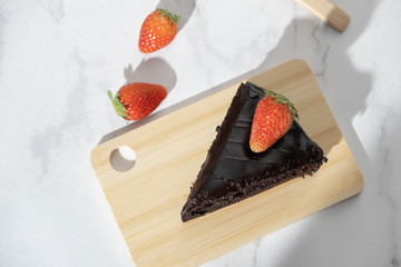 Wooden plate with slice of tasty homemade chocolate fudge cake strawberry on marble table with copy space