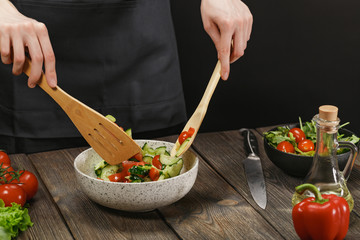 Woman mixing fresh healthy vegetable salad on wooden table. Female hands with copyspace.