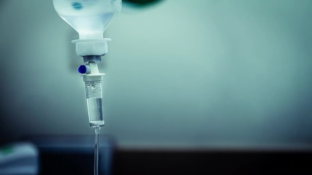 Cinemagraph of a fluid intravenous saline drip in a hospital room. Close up on Set IV fluid intravenous drop saline on a dark blue light background. Loop, selective focus, and copy space.