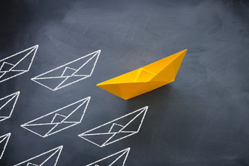 Leadership concept with paper boat on blackboard background. One leader ship leads other ships.