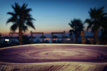 background Image of wooden table in front of abstract blurred tropical palms at sunset lights