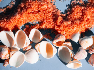 Orange bath salt in a saucer with shells on a holb background with a shadow from a tropical plant....