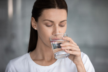 Woman drinks still water close up portrait. Quench thirst, water balance and weight control, caring of skin and body, hangover relief, body refreshment, energy recovery, dehydration prevention concept