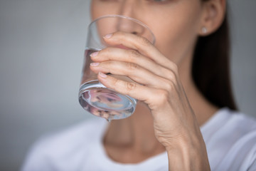 Close up focus on female hand holding glass drinking still clear water. Millennial thirsty...