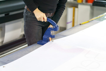 Woman assembles advertising banner with eyelet press