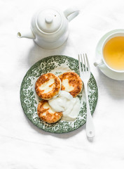 Breakfast served table - cottage cheese pancakes with sour cream, green tea on a light background, top view