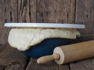 Homemade food.Airy yeast dough in a blue bowl on a wooden background with a rolling pin.