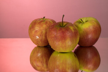 Three red apples on mirroring table on mirror red background with reflection isolated close up