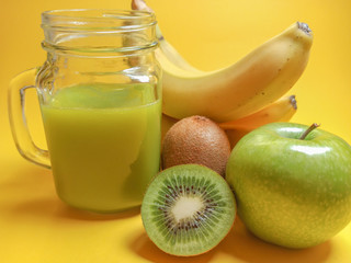Green healthy smoothie in glass jar: banana, kiwi, green apple. Healthy drink on yellow background.