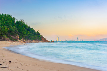 Quy Nhon city panorama from sand beach famous tourism destination in Vietnam. Quy Nhon bay soft sea waves long exposure effect. Sunset light beyond skyscrapers and town skyline.
