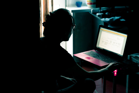 Woman Working On A Laptop In A Dark Room. Woman With Glasses Uses Laptop For Work