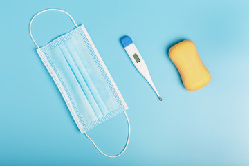 electric thermometer, soap and surgical medical mask on a blue background. concept of protection against coronavirus during a pandemic and quarantine. top view, flat lay.
