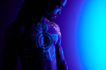 portrait of young black man with colorful ethnic fluorescent prints on his muscular body, shirtless guy posing at camera, colorful makeup and body art