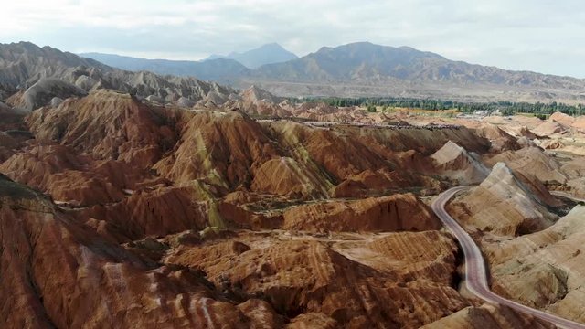 Aerial Top View of Rainbow Mountains Geological Park. Stripy Zhangye Danxia Landform Geological Park in Gansu Province, China. Flying Drone Picture of Tourist Buses on a Road in Valley on a Sunny Day.